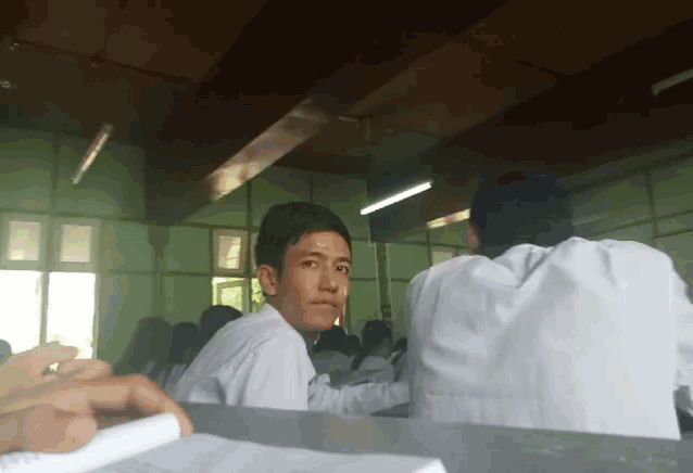 a boy in a white shirt sits in a classroom with other students