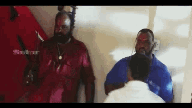 a group of men are standing next to each other in a room and one of them is wearing a red shirt .