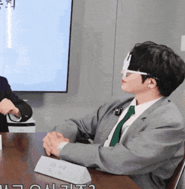 a man in a suit and tie sits at a table with a name tag that says l