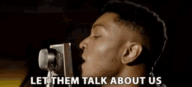 a man singing into a microphone with the words " let them talk about us " below him