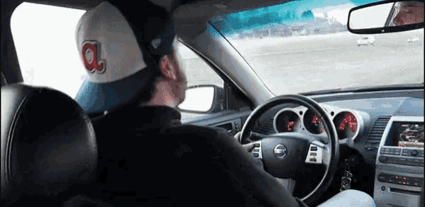 a man wearing an a hat is driving a nissan car