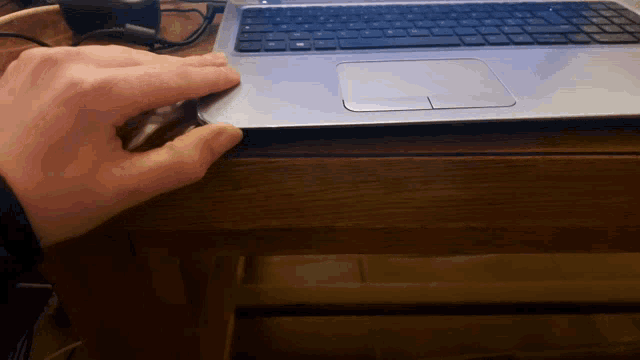 a person 's hand is reaching into a laptop on a wooden desk
