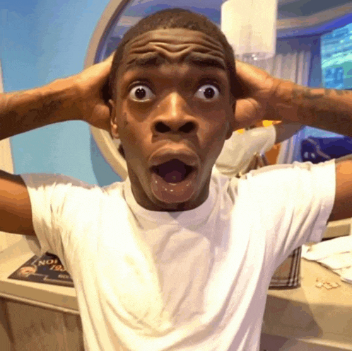 a man in a white shirt is making a surprised face with his hands on his head