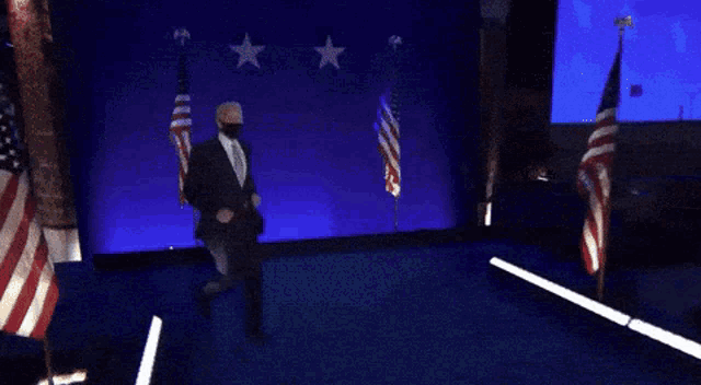 a man in a suit and tie is dancing on a stage with american flags in the background