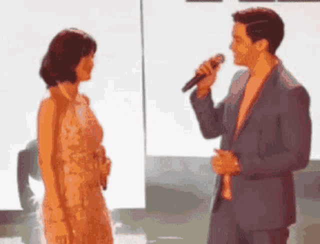 a man is singing into a microphone while standing next to a woman in a dress .