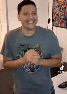 a man wearing a t-shirt with a hulk on it is smiling and clapping his hands in a room .