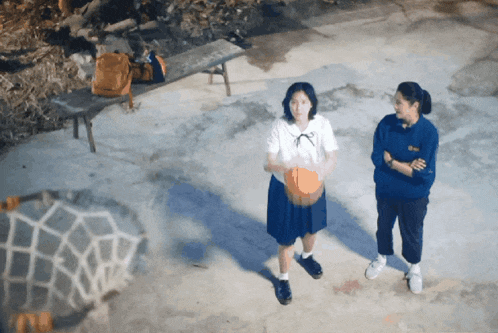 a girl holding a basketball stands next to another girl wearing a blue shirt that says ' ucsd '