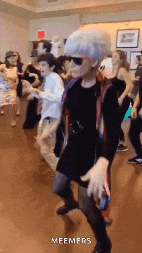 a group of people are dancing in a room and one of them is wearing sunglasses and a wig .