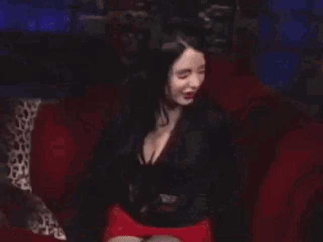 a woman is sitting on a red couch wearing a black top and red skirt .