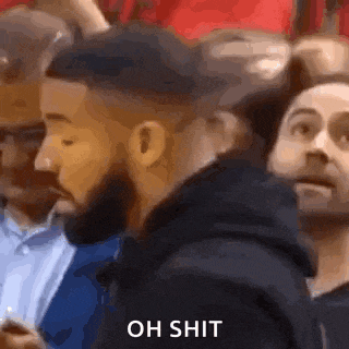 a group of men are sitting in a stadium watching a game and one of them is holding a cell phone .