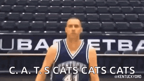 a basketball player in a blue jersey is standing in front of empty bleachers .