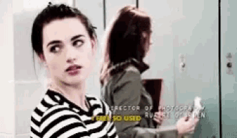 two women are standing next to each other in front of a locker . one of the women is wearing a striped shirt .