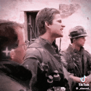 a man in a military uniform is standing next to a man in a helmet and talking to another man .