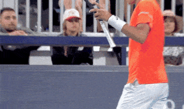 a man in an orange shirt is holding a tennis racquet in his hand