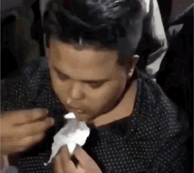 a man in a black shirt is holding a napkin to his nose .