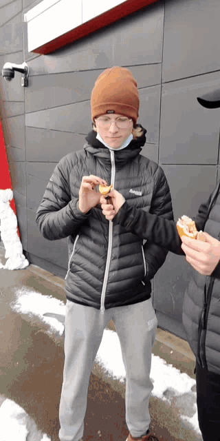a person wearing a black jacket and a brown beanie eating a sandwich