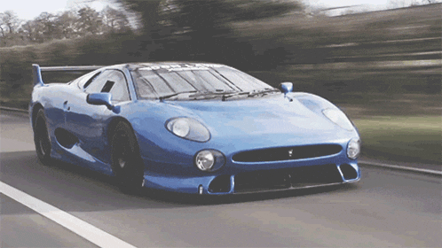 a blue sports car is driving down a road with trees in the background
