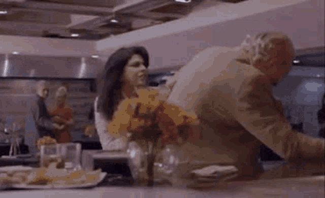 a woman is sitting at a table in a kitchen with a vase of flowers in the background .