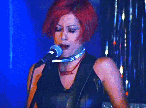 a woman with red hair singing into a microphone with a choker that says devil