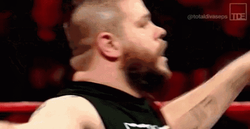 a wrestler is standing in a ring with his arms outstretched and screaming .