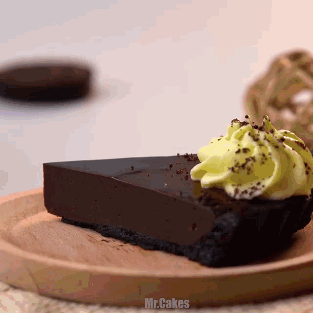 a slice of chocolate cake with yellow frosting on a wooden plate with mr.cakes written on the bottom