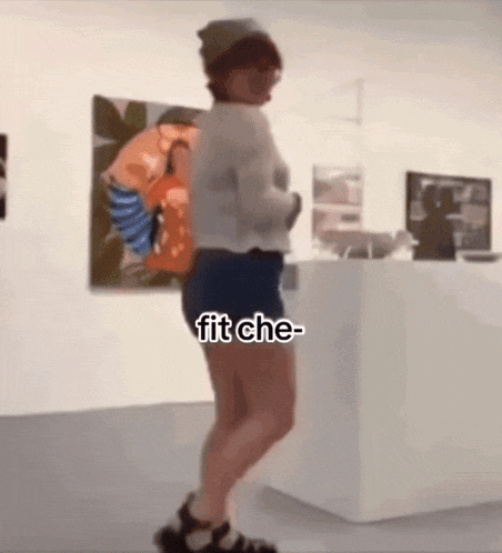 a woman wearing shorts and a hat is dancing in front of a painting that says " fit che "