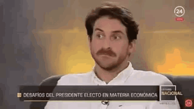 a man with a mustache is sitting on a couch in front of a television .