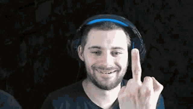 a man with a beard is wearing headphones and making a middle finger sign .