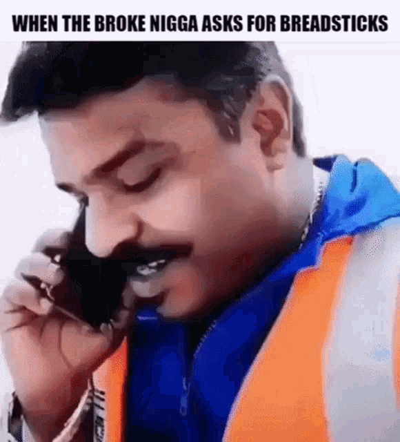 a man is talking on a cell phone while wearing an orange vest and a blue jacket .
