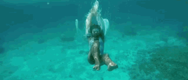 a woman in a white dress is swimming underwater .