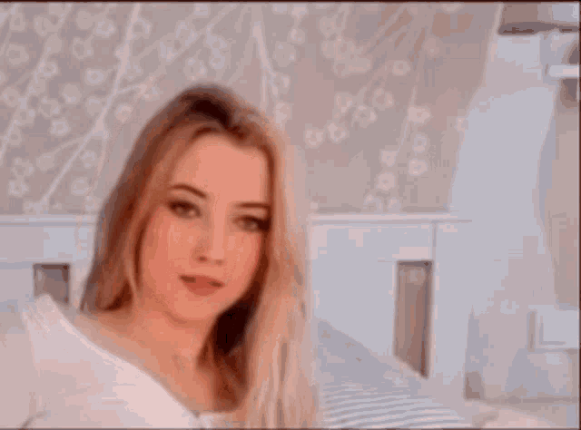 a woman is sitting on a bed with a white headboard looking at the camera .
