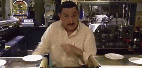 a man in a white shirt is standing behind a counter with plates on it .