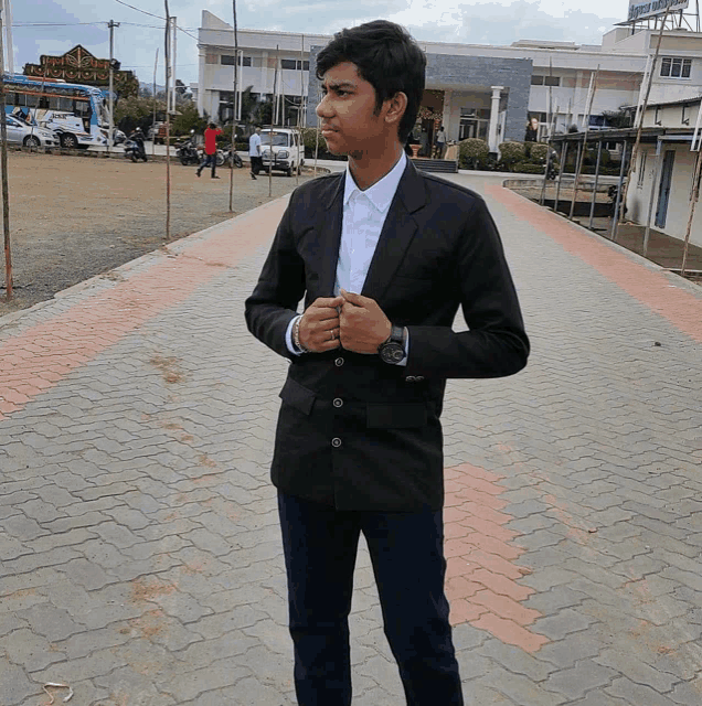 a young man in a black jacket and white shirt stands in front of a building that says ' hotel ' on the top