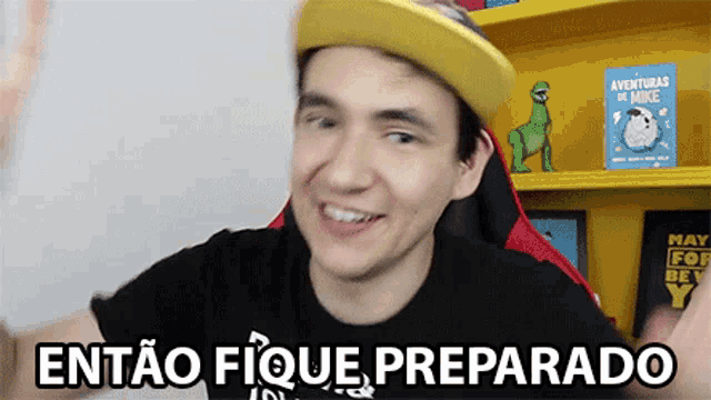 a man wearing a yellow hat and a black shirt is smiling and says " então fique preparado "