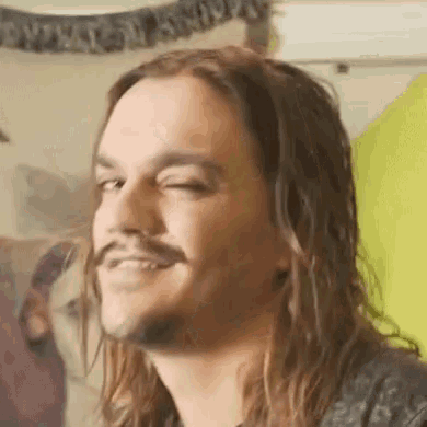 a man with long hair and a mustache is smiling .