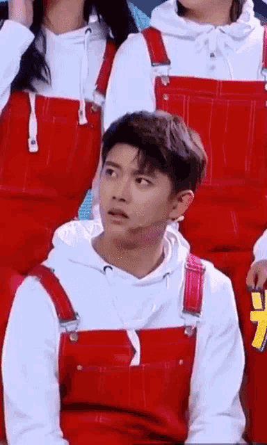 a man wearing red overalls and a white hoodie is sitting in a group of people .