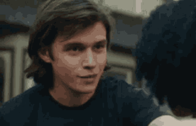 a young man in a blue shirt is looking at another young man in a white shirt .
