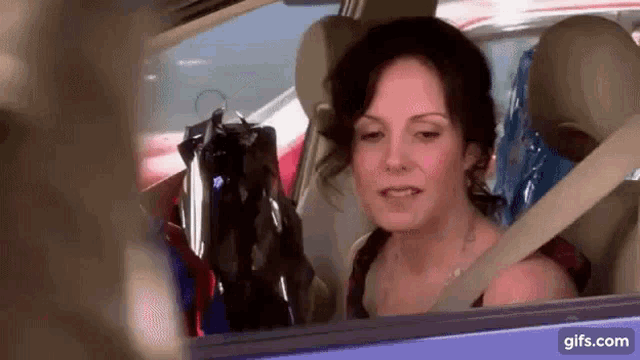 a woman is sitting in the back seat of a car with clothes hanging from the back seat .