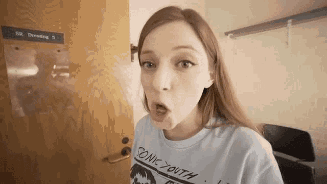 a woman wearing a sonic youth shirt is standing in front of a door .