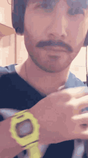 a man with a beard and mustache is wearing headphones and a yellow watch on his wrist .