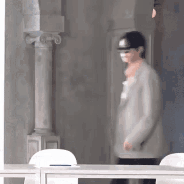 a man with a mask on his face is walking in a room with columns .