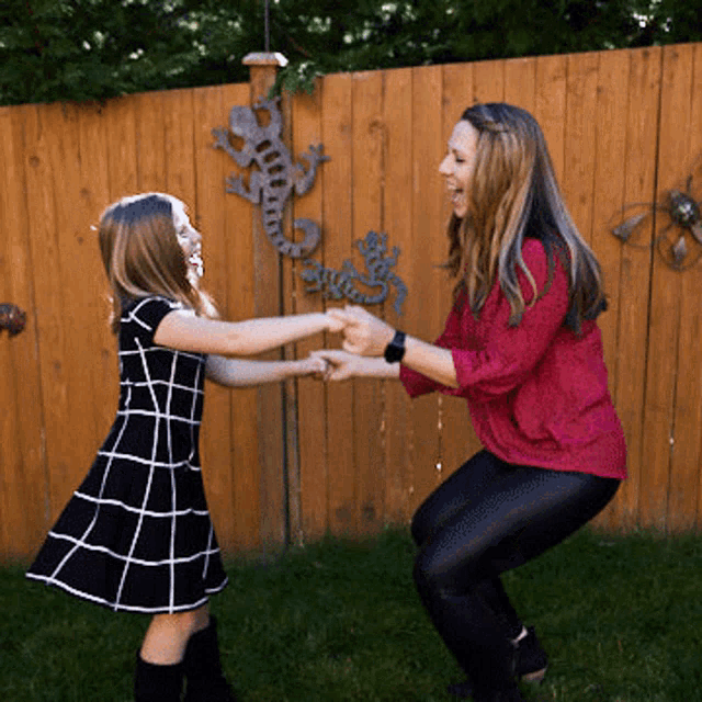 a woman in a red shirt is squatting next to a little girl in a black dress