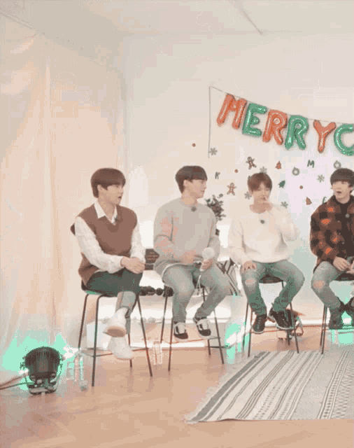a group of young men sit in front of a merry christmas sign
