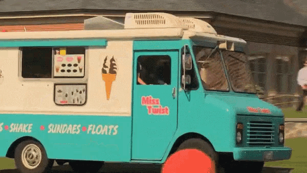 a blue and white miss twist ice cream truck is parked in front of a building