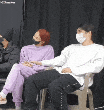 two men wearing masks are sitting next to each other in chairs holding hands .