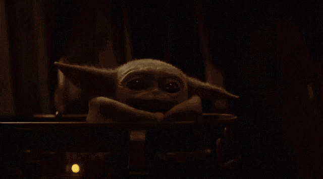 a baby yoda is sitting in a dark room with a red light behind it .