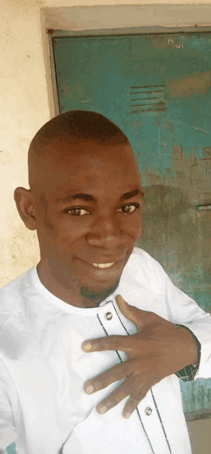 a man in a white shirt holds his hand to his chest and smiles