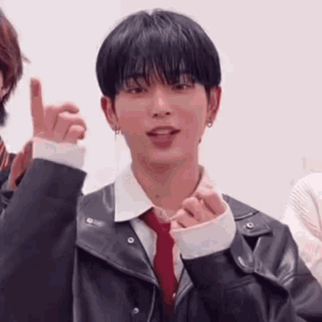 a young man wearing a leather jacket and tie is making a heart with his hands .