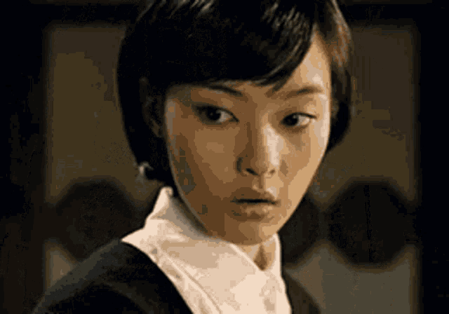 a woman with short black hair and a white shirt is looking at the camera .
