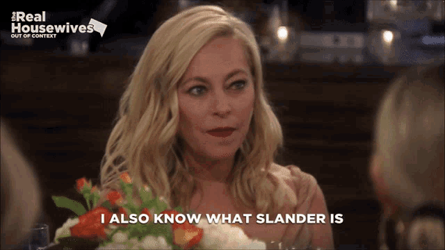 a woman is sitting at a table with a bouquet of flowers and says " i also know what slander is "